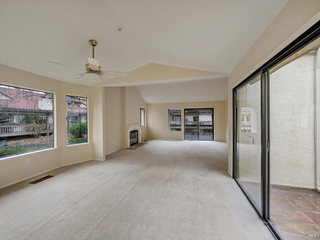 unfurnished living room with visible vents, ceiling fan, carpet floors, vaulted ceiling, and a glass covered fireplace