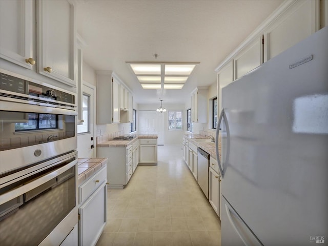 kitchen featuring white cabinets, an inviting chandelier, a sink, stainless steel appliances, and tile countertops
