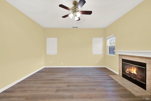 unfurnished living room featuring a tiled fireplace, ceiling fan, and wood-type flooring