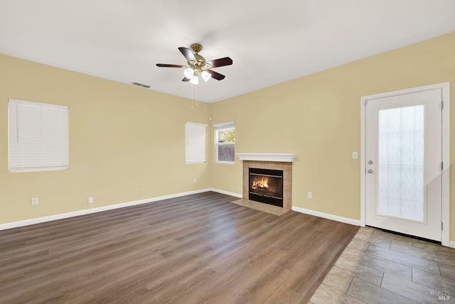 unfurnished living room with hardwood / wood-style floors, ceiling fan, and a tiled fireplace