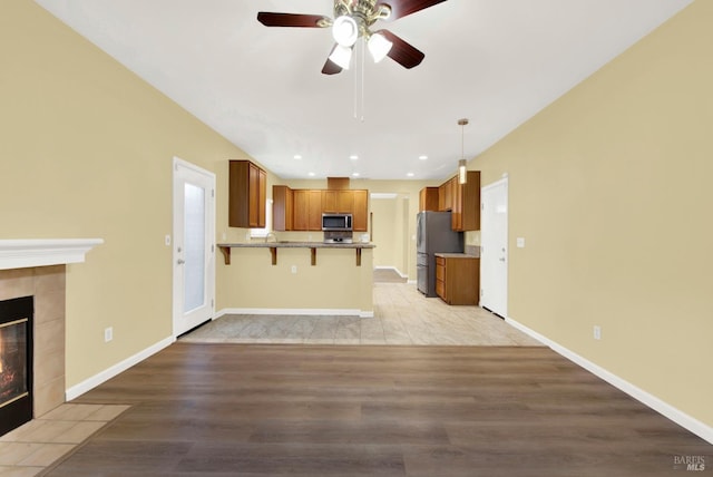 kitchen with appliances with stainless steel finishes, decorative light fixtures, light hardwood / wood-style floors, kitchen peninsula, and a breakfast bar area