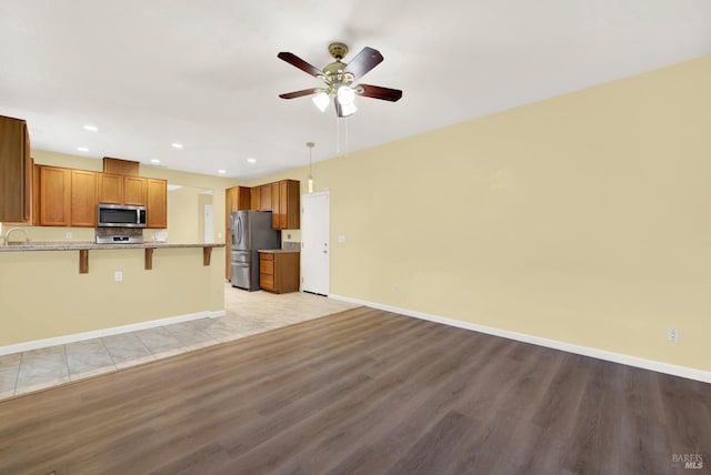 kitchen featuring a breakfast bar, ceiling fan, appliances with stainless steel finishes, decorative light fixtures, and light hardwood / wood-style floors