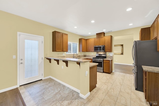 kitchen featuring sink, light stone counters, kitchen peninsula, a kitchen bar, and appliances with stainless steel finishes