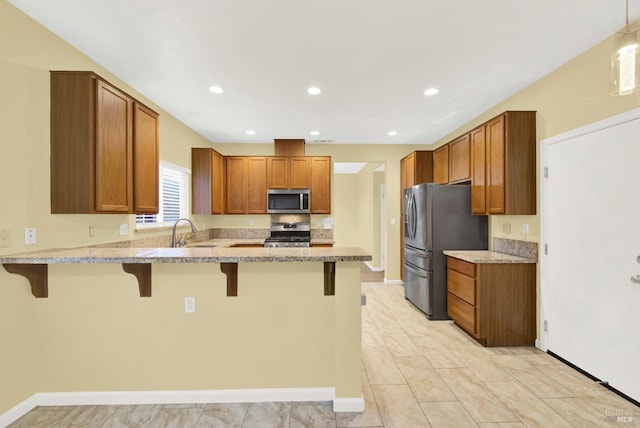 kitchen featuring a kitchen bar, appliances with stainless steel finishes, kitchen peninsula, light stone countertops, and sink