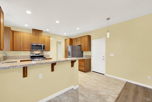 kitchen with light stone countertops, sink, hanging light fixtures, stainless steel appliances, and a kitchen bar