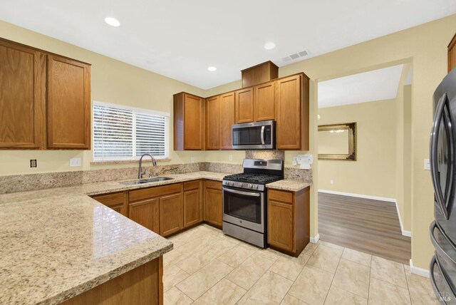 kitchen featuring sink, light stone countertops, stainless steel appliances, and light wood-type flooring