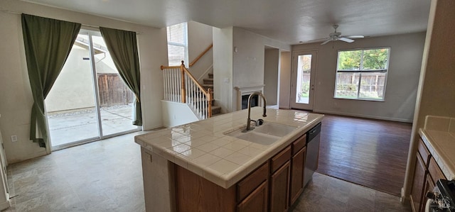 kitchen featuring ceiling fan, sink, stainless steel dishwasher, wood-type flooring, and a kitchen island with sink