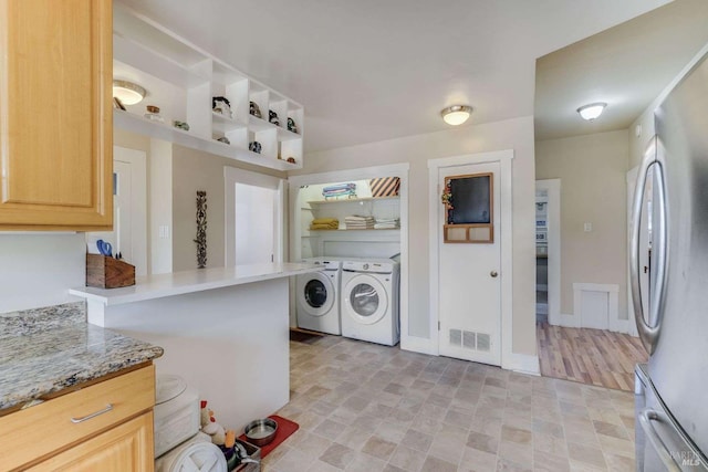 kitchen featuring light stone countertops, light brown cabinets, independent washer and dryer, and stainless steel refrigerator