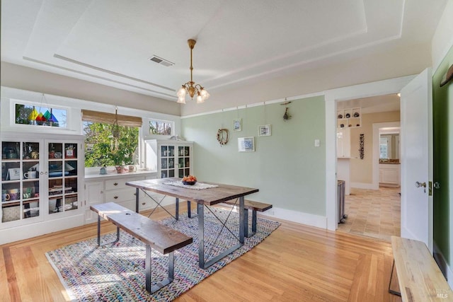 dining area featuring a notable chandelier, light hardwood / wood-style floors, and a tray ceiling