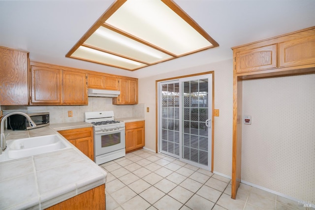 kitchen with light tile patterned floors, tile counters, a sink, white range with gas stovetop, and under cabinet range hood