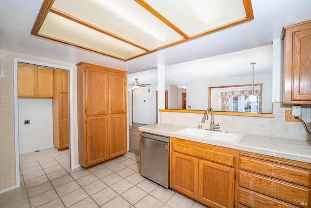 kitchen featuring tile countertops, stainless steel dishwasher, a ceiling fan, brown cabinetry, and a sink