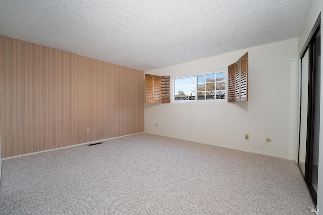 carpeted spare room featuring a textured ceiling, visible vents, and wallpapered walls