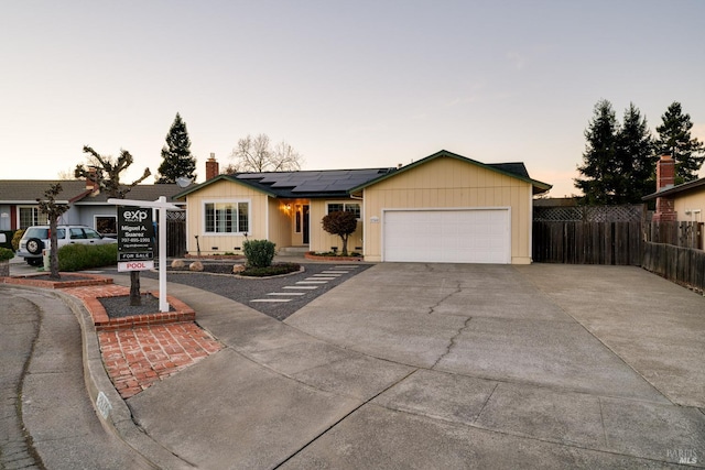 single story home featuring roof mounted solar panels, fence, driveway, and an attached garage