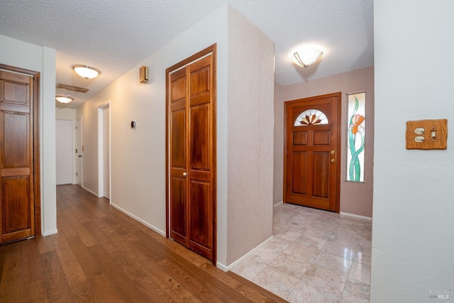 foyer entrance with a textured ceiling, light wood-style flooring, and baseboards