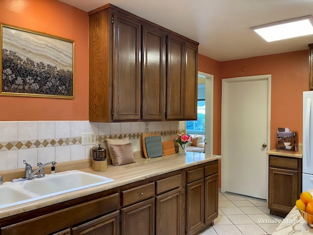 kitchen with sink, white fridge, light tile patterned flooring, tile walls, and dark brown cabinets