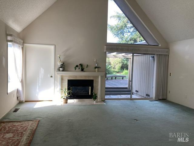 unfurnished living room with high vaulted ceiling, a textured ceiling, and light carpet