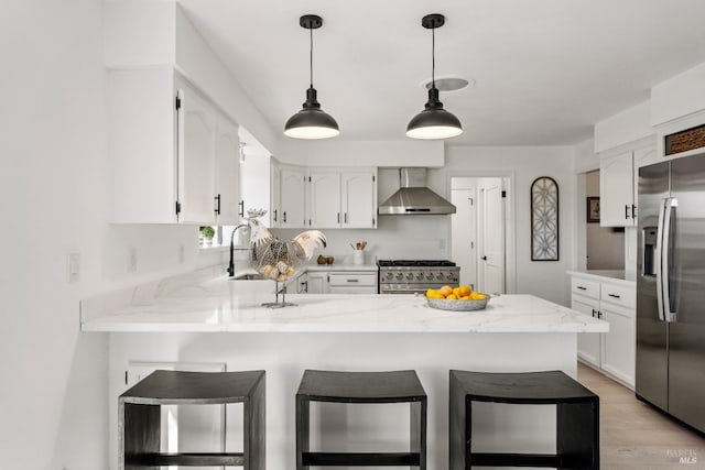 kitchen with light wood-type flooring, wall chimney exhaust hood, stainless steel appliances, white cabinets, and a breakfast bar area