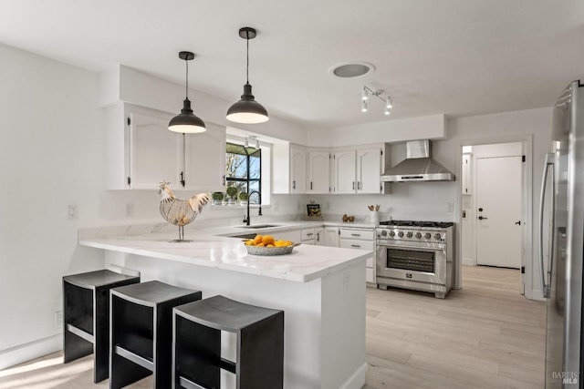 kitchen with kitchen peninsula, stainless steel appliances, wall chimney range hood, and light hardwood / wood-style floors