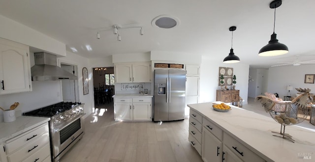 kitchen featuring light hardwood / wood-style flooring, wall chimney exhaust hood, ceiling fan, appliances with stainless steel finishes, and white cabinetry