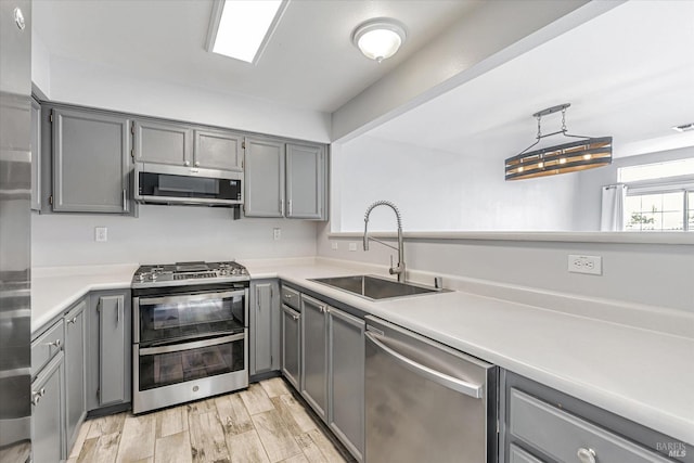 kitchen with sink, stainless steel appliances, pendant lighting, light hardwood / wood-style floors, and gray cabinets