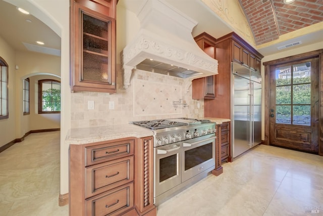 kitchen featuring high end appliances, tasteful backsplash, light stone counters, brick ceiling, and custom exhaust hood