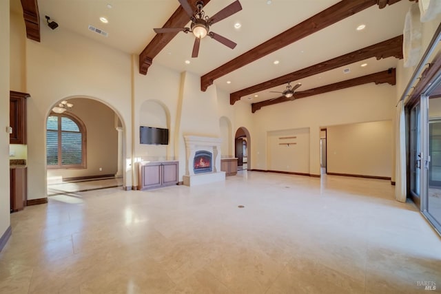 unfurnished living room with beam ceiling, ceiling fan, and a towering ceiling