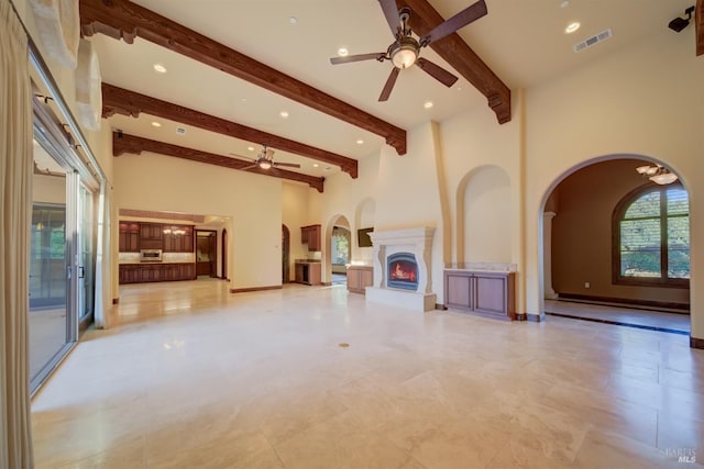 unfurnished living room featuring beamed ceiling, ceiling fan, a high ceiling, and a baseboard radiator