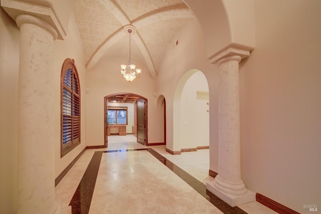 corridor featuring ornate columns, high vaulted ceiling, and a chandelier