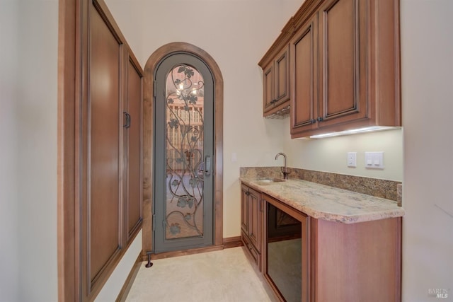 bar with wine cooler, light stone countertops, and sink