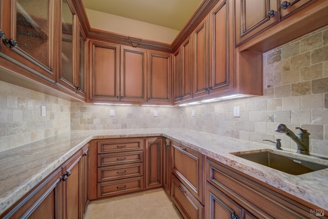 kitchen with backsplash, light tile patterned flooring, light stone countertops, and sink