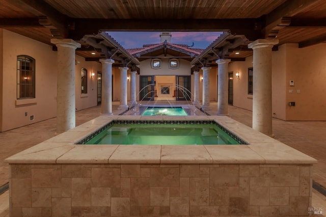 pool at dusk featuring pool water feature and an in ground hot tub