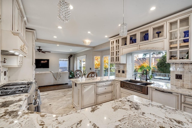 kitchen featuring backsplash, cream cabinets, hanging light fixtures, ceiling fan, and stainless steel range