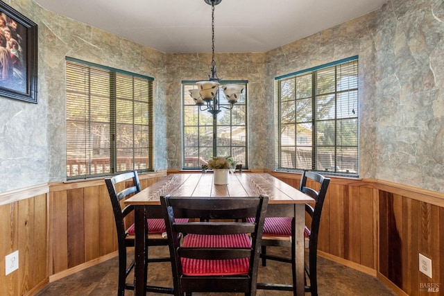 dining space featuring an inviting chandelier, plenty of natural light, and wood walls