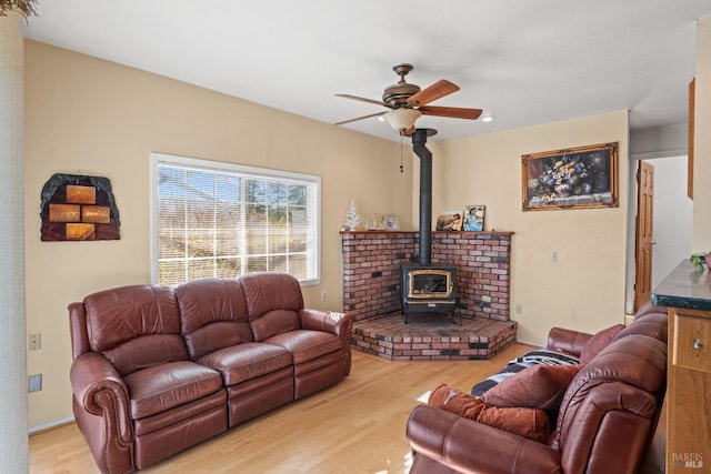 living room featuring light wood-type flooring, a wood stove, and ceiling fan