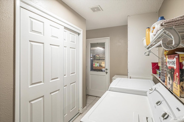 laundry area with light tile patterned flooring, washing machine and clothes dryer, and a textured ceiling