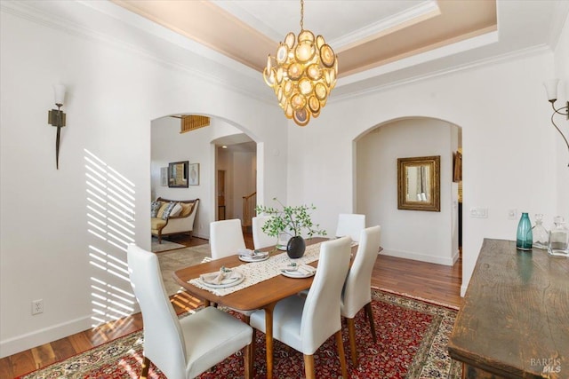 dining room featuring a notable chandelier, ornamental molding, hardwood / wood-style floors, and a raised ceiling