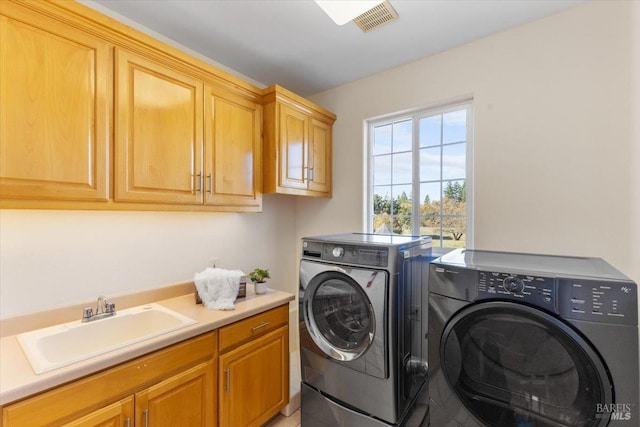 clothes washing area with sink, washing machine and dryer, and cabinets