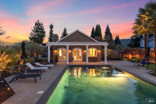 pool at dusk with a patio, an outbuilding, and a pergola