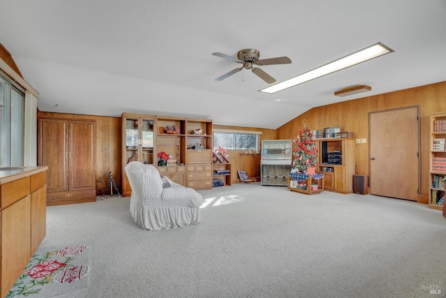 interior space featuring ceiling fan, light carpet, wooden walls, and vaulted ceiling