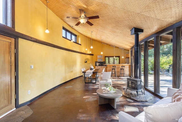 sunroom with plenty of natural light, ceiling fan, a wood stove, and vaulted ceiling