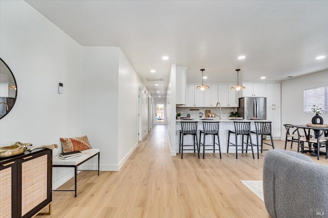 kitchen featuring a kitchen bar, light wood-type flooring, decorative light fixtures, white cabinetry, and stainless steel refrigerator