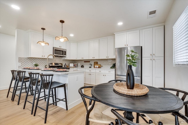 kitchen featuring white cabinetry, pendant lighting, light wood-type flooring, and appliances with stainless steel finishes