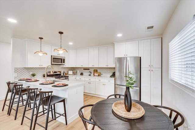 kitchen with white cabinetry, stainless steel appliances, hanging light fixtures, and light hardwood / wood-style flooring