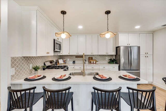 kitchen featuring appliances with stainless steel finishes, decorative light fixtures, light hardwood / wood-style flooring, and sink