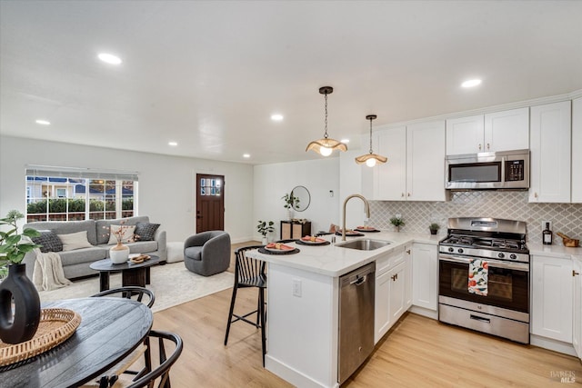 kitchen with kitchen peninsula, stainless steel appliances, sink, light hardwood / wood-style flooring, and hanging light fixtures