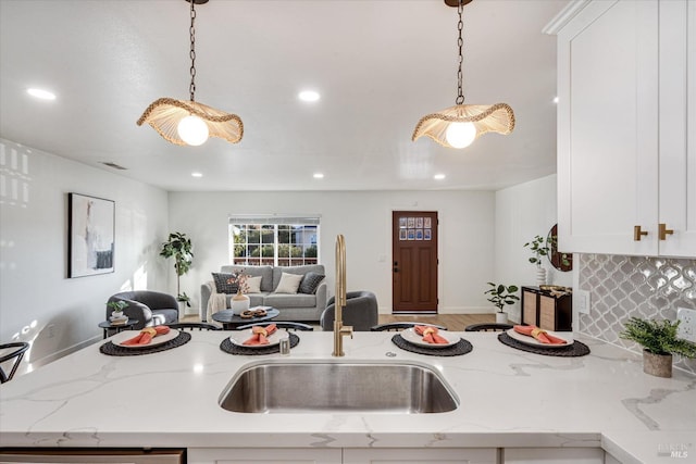 kitchen featuring sink, hanging light fixtures, light stone counters, backsplash, and white cabinets