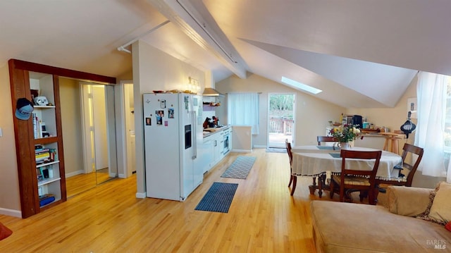 kitchen with stainless steel oven, white refrigerator with ice dispenser, white cabinets, vaulted ceiling with skylight, and light hardwood / wood-style floors