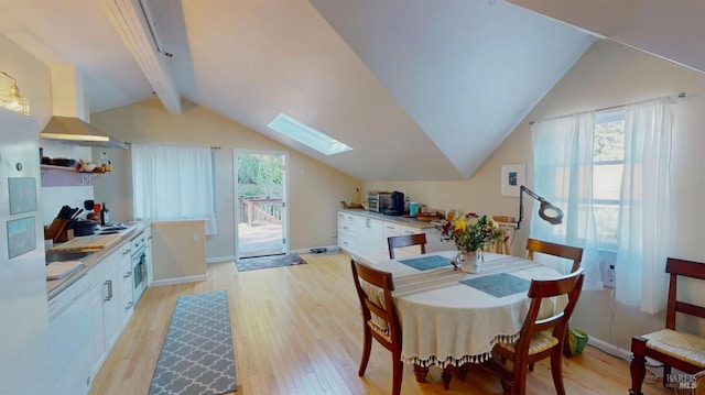 dining room with vaulted ceiling with skylight and light hardwood / wood-style flooring