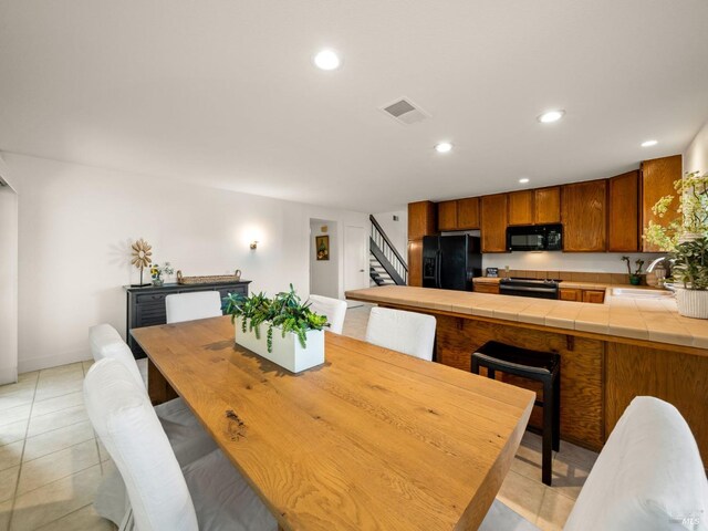 kitchen featuring light tile patterned floors, tile countertops, and black refrigerator with ice dispenser