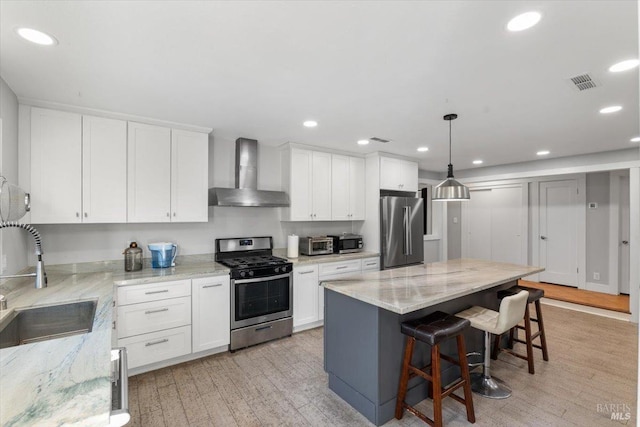 kitchen featuring a center island, sink, wall chimney exhaust hood, light wood-type flooring, and stainless steel appliances